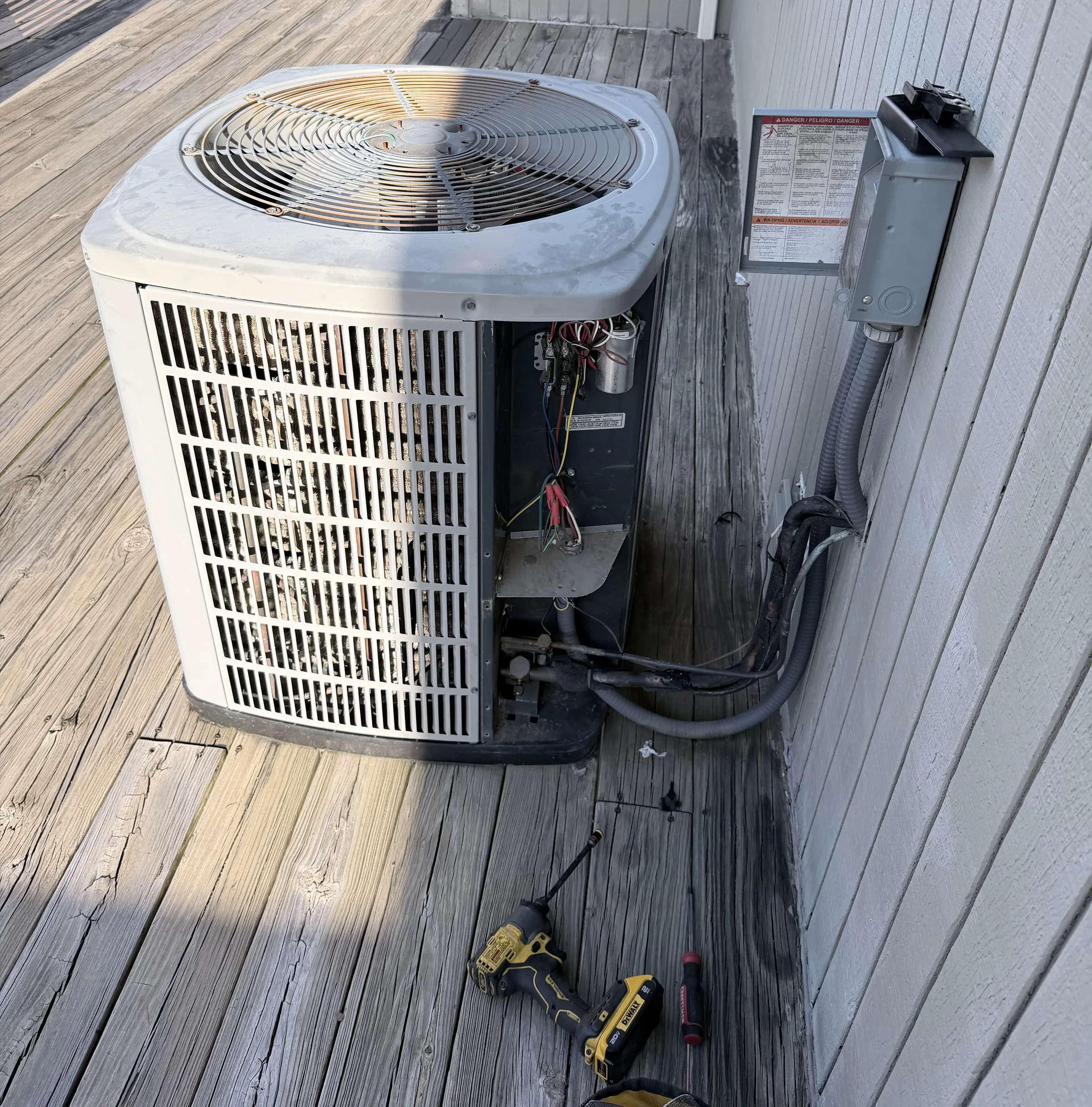 An outdoor condensing unit with its service panel removed and hand tools resting on the deck beside it.