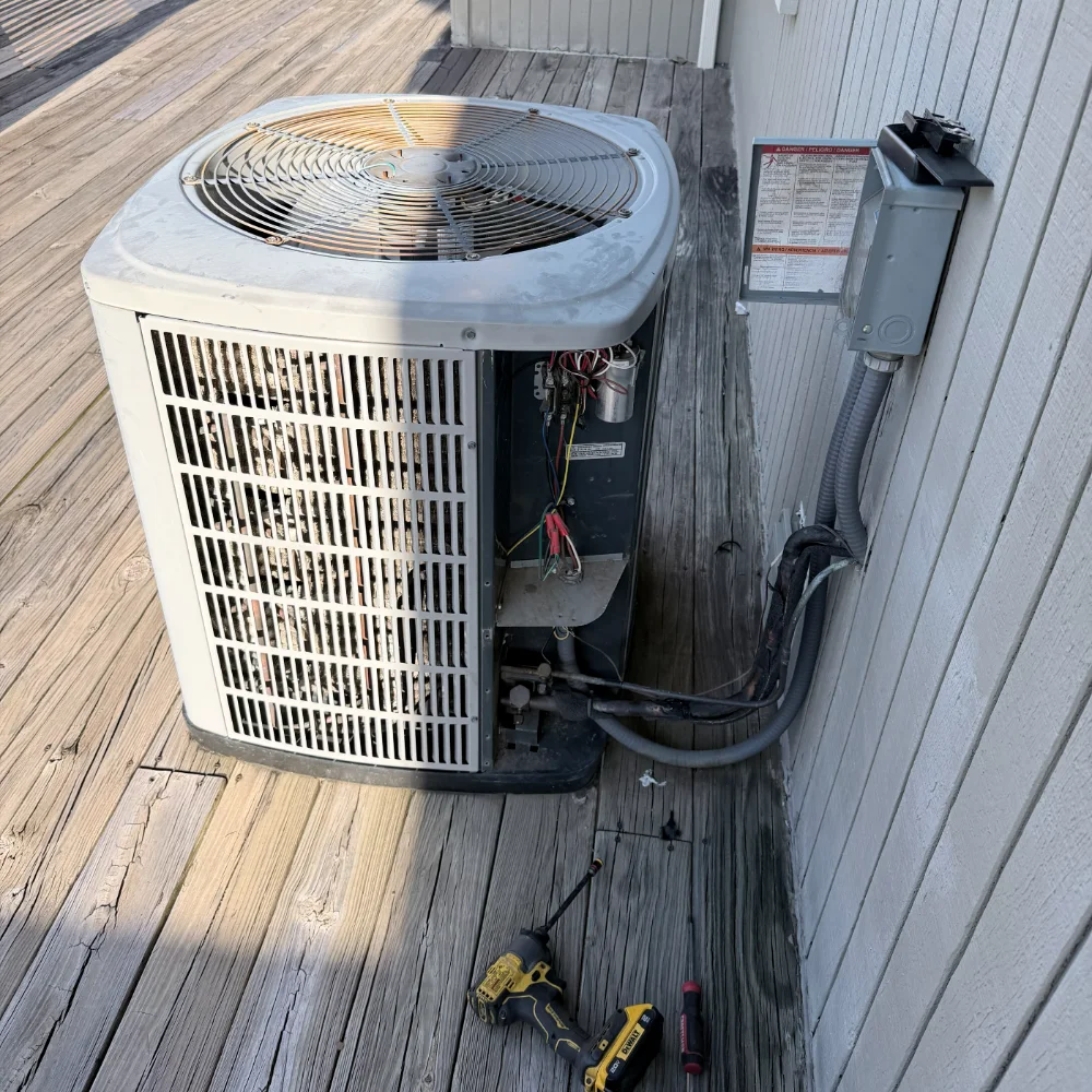 An outdoor condensing unit opened for diagnosis with gauges, meter leads and hand tools arranged beside it.