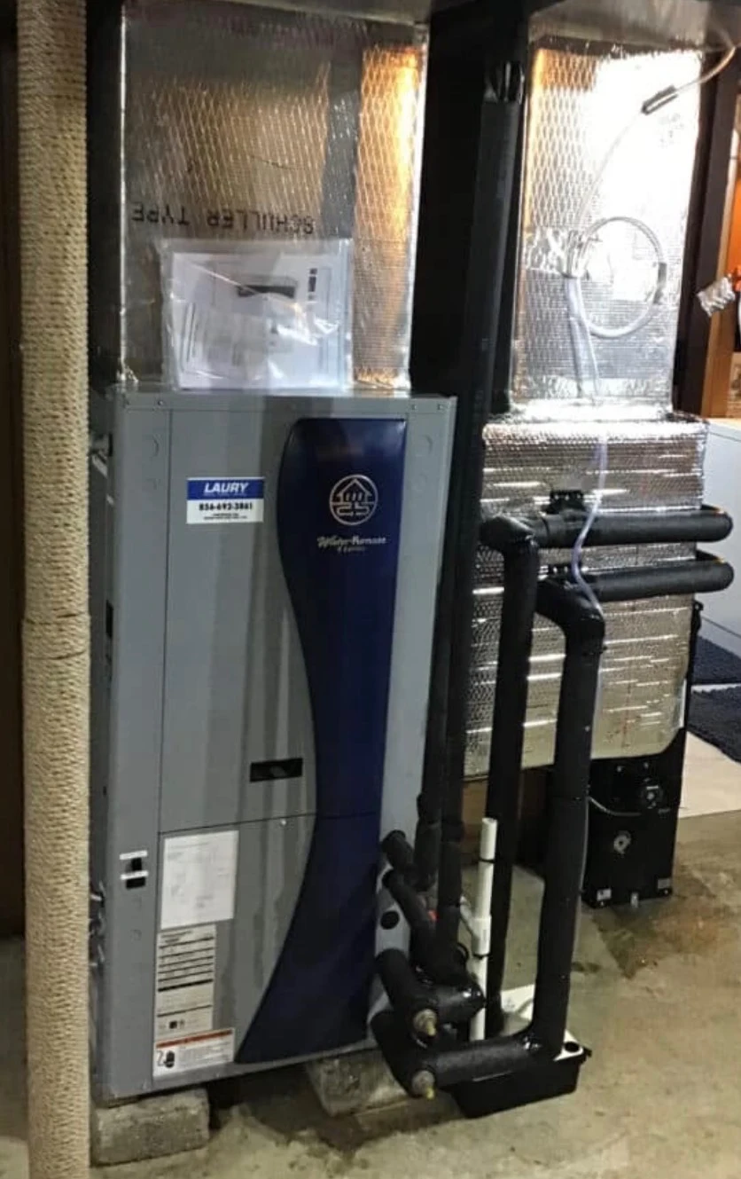 A geothermal heat pump installed indoors, with insulated ductwork above it and loop piping running to the unit.