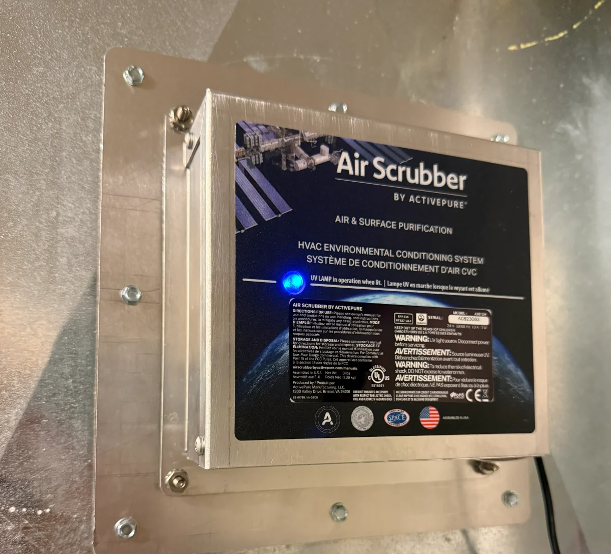 An air purification unit mounted on the ductwork of an indoor HVAC system with its indicator lamp lit.