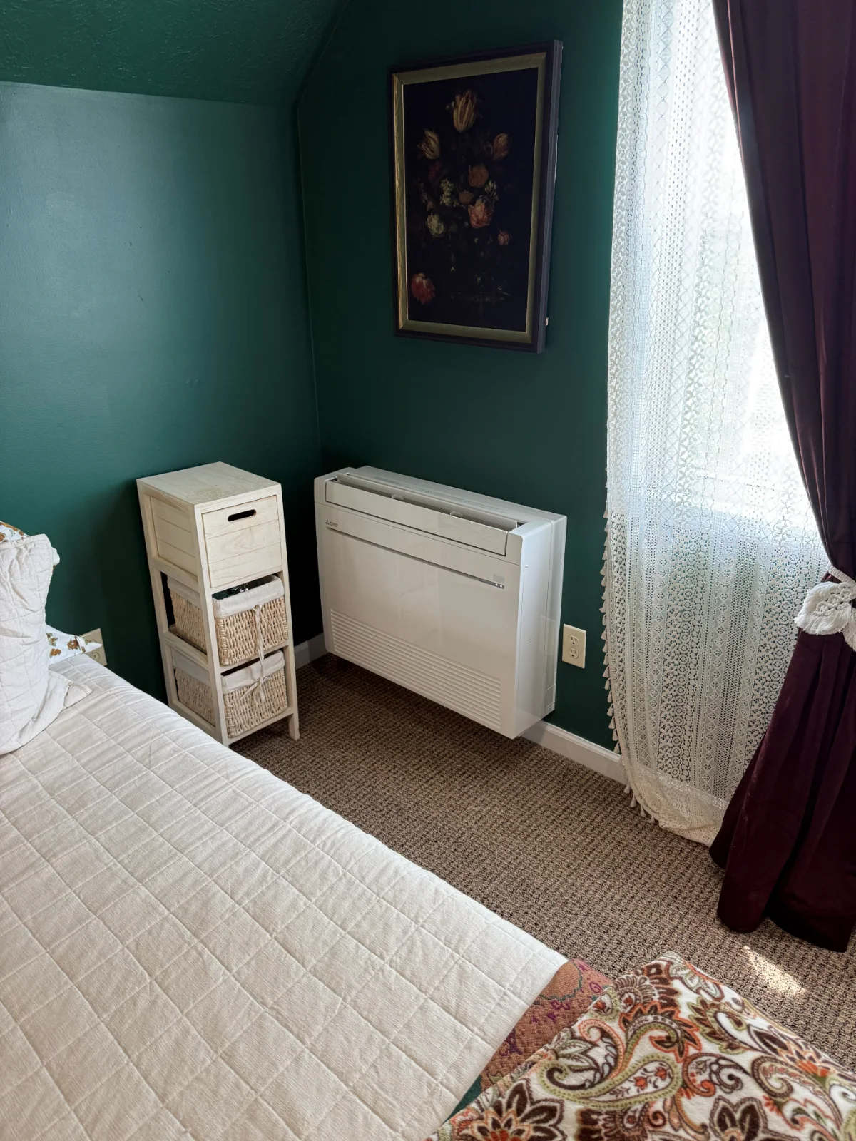 A white floor-mounted ductless indoor unit installed against a dark green bedroom wall.