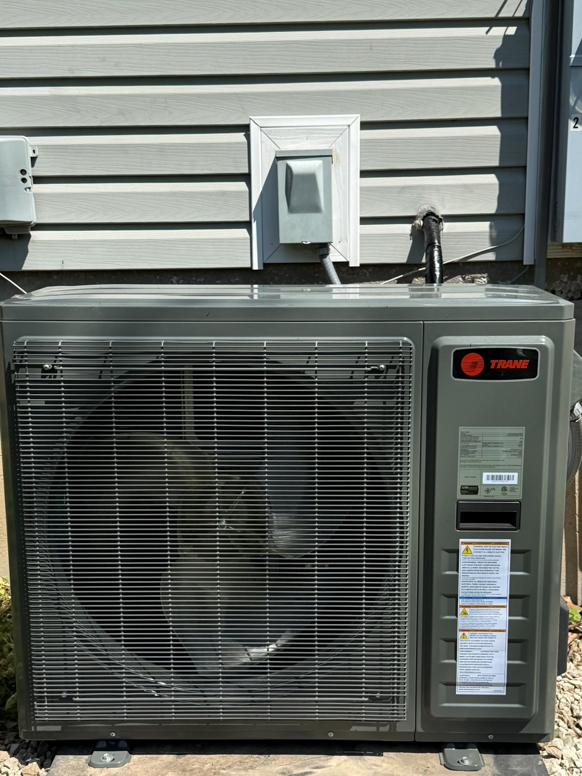 An outdoor condensing unit raised above a weathered wood deck beside light siding.