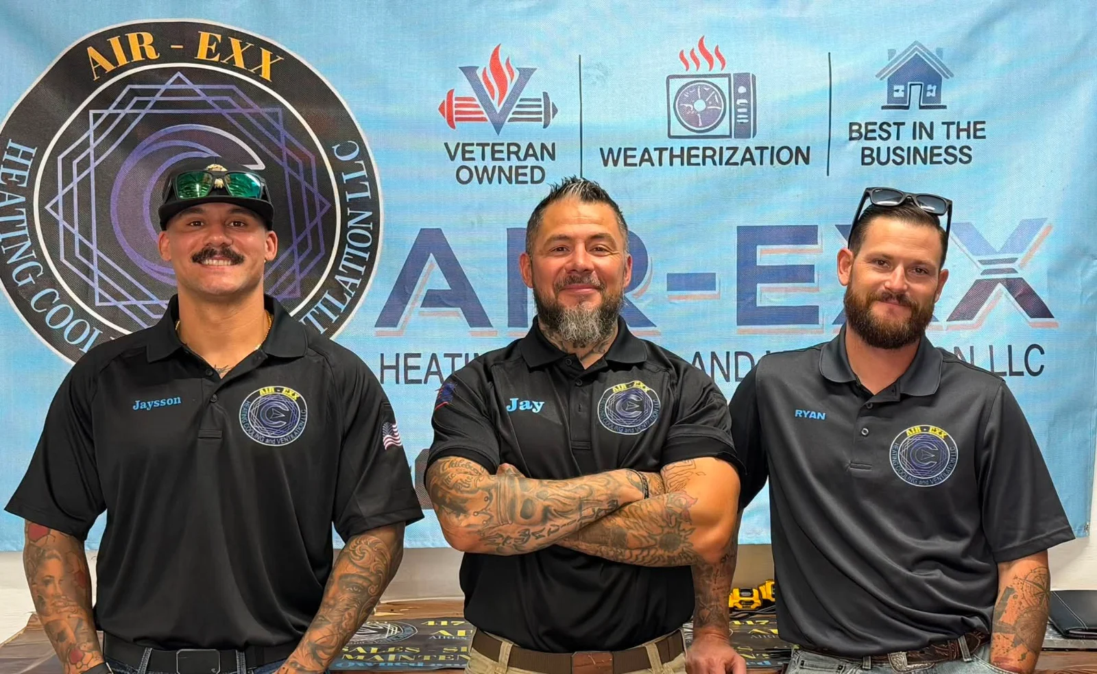 Three Air-Exx owners standing together in matching company shirts in front of an Air-Exx banner.